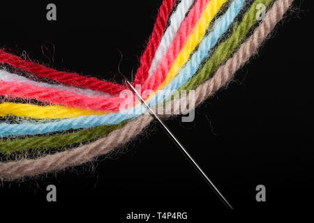 On a black background, several bright multicolored woolen threads are pass through the eye of the needle. Close-up Stock Photo