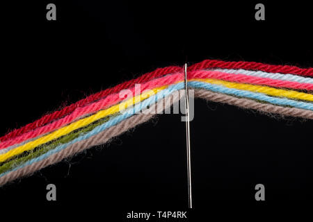 On a black background, several bright multicolored woolen threads are pass through the eye of the needle. Close-up Stock Photo