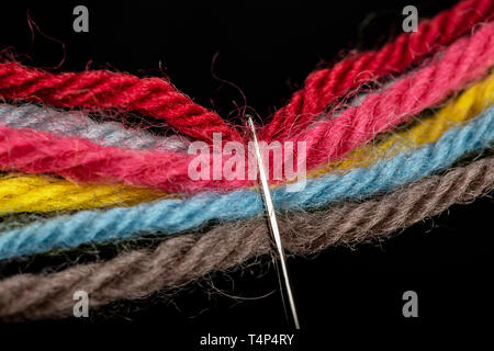 On a black background, several bright multicolored woolen threads are pass through the eye of the needle. Close-up Stock Photo