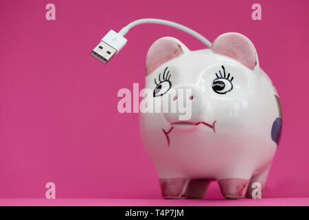 White porcelaine piggy bank with USB cable coming out of back on pink bacgdrop, sceptical look sideways. Stock Photo