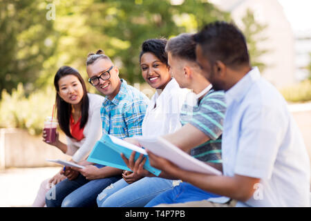 education, international and people concept - group of happy exchange students with notebook and takeaway drinks talking outdoors Stock Photo