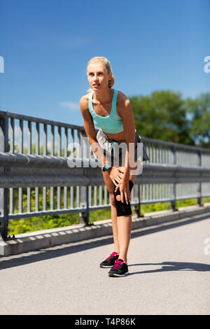 fitness, sport, exercising and healthy lifestyle concept - young woman with knee support brace on leg outdoors Stock Photo