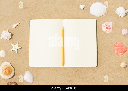 vacation, travel and summer concept - notebook with pencil and seashells on beach sand Stock Photo