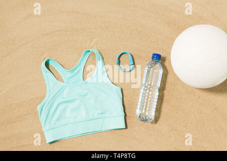 sport, summer and objects concept - sports top, ball, fitness tracker and water bottle on beach sand Stock Photo