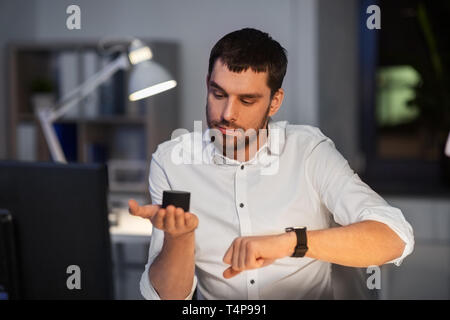 business, technology and internet of things concept - businessman using smart speaker and watch at night office Stock Photo