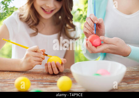 easter, holidays and people concept - happy smiling girl with mother coloring eggs over green natural background Stock Photo