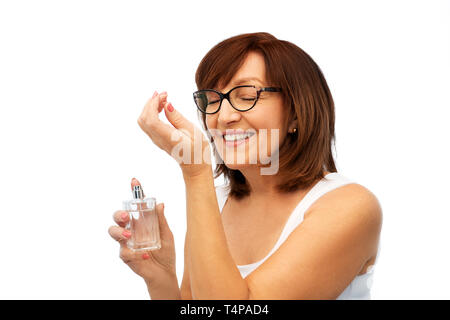 perfumery, beauty and luxury concept - happy smiling senior woman smelling perfume from her wrist over white background Stock Photo