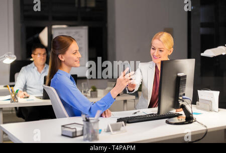 business, deadline and technology concept - businesswomen with smartphone having coffee break late at night office Stock Photo