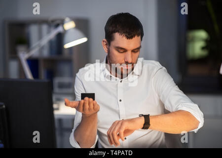 business, technology and internet of things concept - businessman using smart speaker and watch at night office Stock Photo