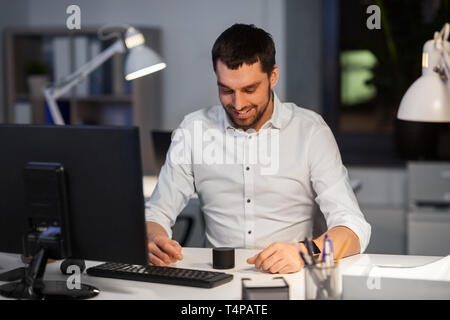 business, technology and internet of things concept - happy businessman using smart speaker at night office Stock Photo