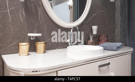 Luxury modern big white faucet mixer on a round sink in a beautiful beige marble bathroom, a large round mirror Stock Photo