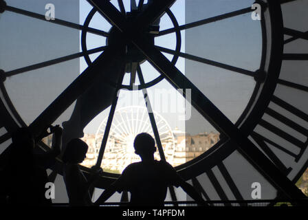 Three tourists in silhouette as they admire the view of the Ferris Wheel from the window behind the huge clock in the d'Orsay museum in Paris France. Stock Photo