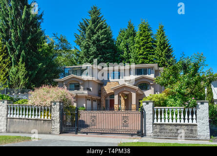 Luxury residential house with double garage and metal gate in front. Beautiful house in suburb of Vancouver on blue sky background Stock Photo