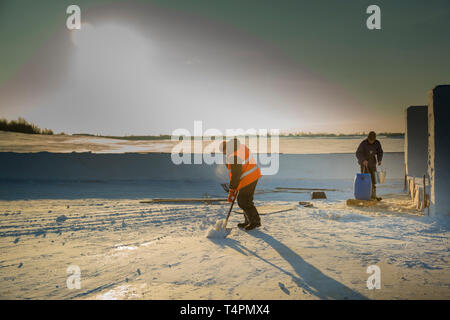 Portrait of a worker in an orange reflective vest snow shoveling on a river ice Stock Photo