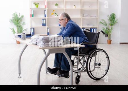 Aged employee in wheelchair working in the office Stock Photo