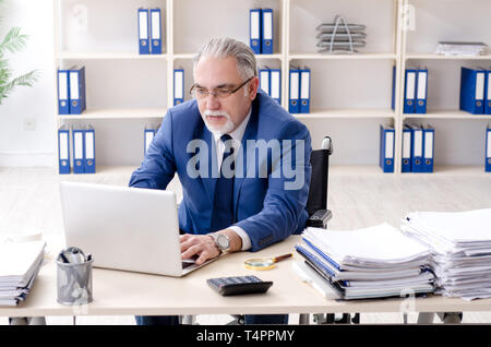 Aged employee in wheelchair working in the office Stock Photo