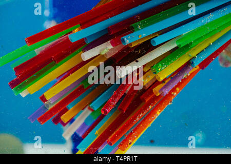 Dangerous plastic straws. Bright toxic straws made of plastic and covered in glitter pieces on blue background Stock Photo