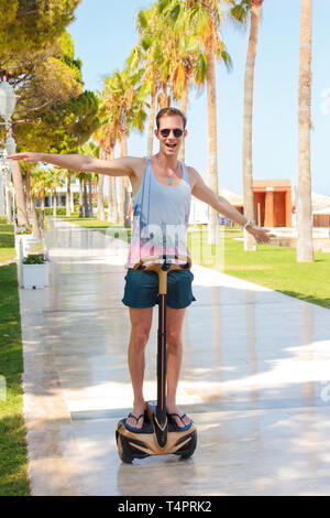 Happy smiling young man on segway. Riding a gyroscooter on a sunny summer palm alley Stock Photo