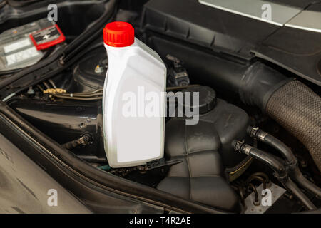 Spare part for car engine one liter bottle or can of lubricant in gray with red cap on a background with under hood compartment. Maintenance and oil c Stock Photo