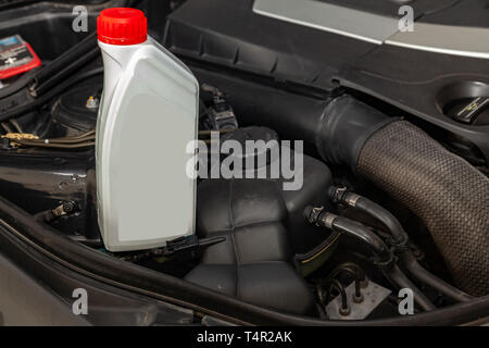 Spare part for car engine one liter bottle or can of lubricant in gray with red cap on a background with under hood compartment. Maintenance and oil c Stock Photo