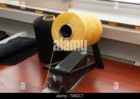 One big yellow bobbin with large mating colored threads in the studio fot interior design workshop on the table with thread stretching towards the cam Stock Photo