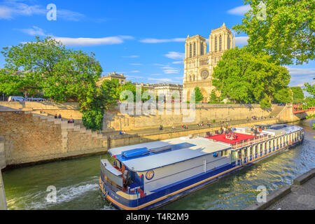 Paris, France - July 1, 2017: Cruise of Bateaux-Mouches boat with tourist during a trip at sunset on River Seine with Cathedral of Notre Dame on the Stock Photo