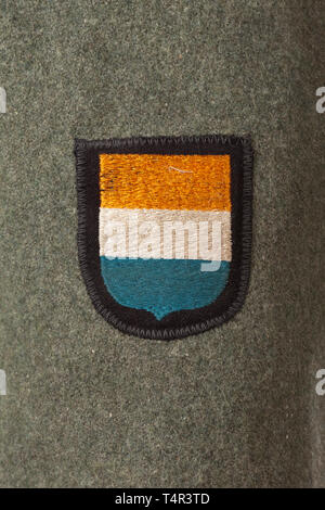 A field tunic M 43 ('two-hole jacket') for an SS member of the 23rd SS Volunteer Panzer Grenadier Division 'Nederland' (Dutch no. 1) Field-grey felt, field-grey painted buttons, machine-stitched sleeve eagle (BeVo issue), the sleeve insignia and collar patches (RZM-embroidered) likewise machine-stitched. Grey inner liner with depot and size stampings. Very rare. historic, historical, 20th century, 1930s, 1940s, Waffen-SS, armed division of the SS, armed service, armed services, NS, National Socialism, Nazism, Third Reich, German Reich, Germany, military, militaria, utensil,, Editorial-Use-Only Stock Photo