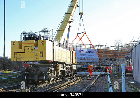 A railway-mounted Kirow crane lifts a temporary scaffolding footbridge into place at Feltham Station, Middlesex during a weekend railway closure. Stock Photo