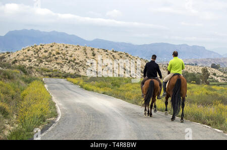 Murcia, Spain, April 18, 2019: Rear view of two men Riding Horses Along a Road in the mountain. Farmer riding horse at mountain roads. Stock Photo