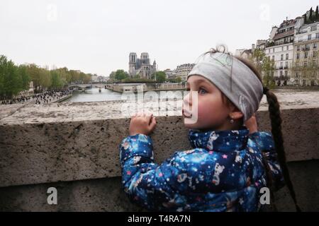 (190418) -- BEIJING, April 18, 2019 (Xinhua) -- A girl reacts while watching the Notre Dame Cathedral after a fire in Paris, France, on April 16, 2019. French President Emmanuel Macron on Tuesday vowed to rebuild Notre Dame Cathedral, devastated by fire on Monday evening, within five years, calling on the French to remain united. In early Monday evening, a fire broke out in the famed cathedral. Online footage showed thick smoke billowing from the top of the cathedral and huge flames between its two bell towers engulfing the spire and the entire roof which both collapsed later. (Xinhua/Gao Jing