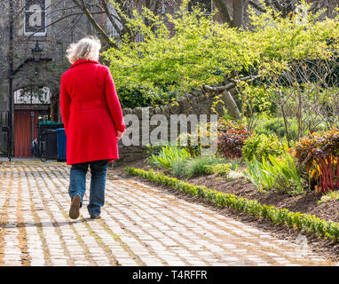 Royal Mile, Edinburgh, Scotland, United Kingdom, 18th April 2019. UK Weather: A woman wearing a red coat strolls through Dunbar Close Gardens on a Spring day Stock Photo