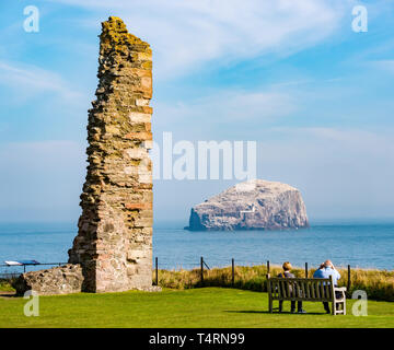 Tantallon Castle, North Berwick, East Lothian, Scotland, United Kingdom, 19th April 2019. UK Weather: Historic Environment Scotland's ruined 14th century castle. The ruined castle with a view of the largest Northern gannet colony on the Bass Rock in the Firth of Forth. The gannets are reuniting and building nests. A couple with binoculars sit on a bench to watch the seabirds Stock Photo