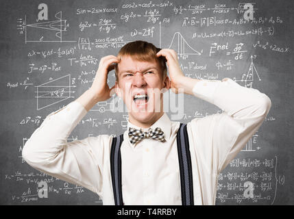 Stressful teenager screaming with panic and keeps hands on head. Emotional redhead boy doing mathematical calculations. Guy wears white shirt and bow  Stock Photo