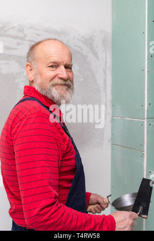 Picture of a senior worker holding a spatula filling in the walls in a new apartment Stock Photo