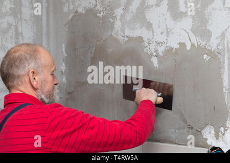Picture of a senior worker holding a spatula filling in the walls in a new apartment Stock Photo