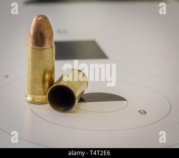 A 9mm bullet with a paper target in the background Stock Photo