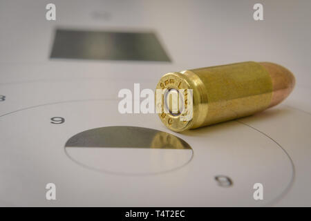 A 9mm bullet with a paper target in the background Stock Photo