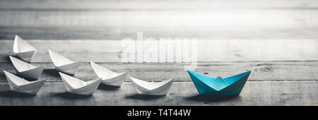Blue Paper Boat Leading A Fleet Of Small White Boats On Wooden Table With Vintage Effect - Leadership Concept Stock Photo