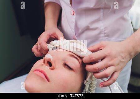 Facial procedures. Nice skilled cosmetician taking off a mask while doing a beauty procedure Stock Photo