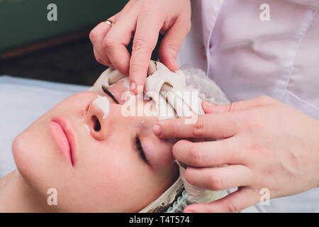 Facial procedures. Nice skilled cosmetician taking off a mask while doing a beauty procedure Stock Photo