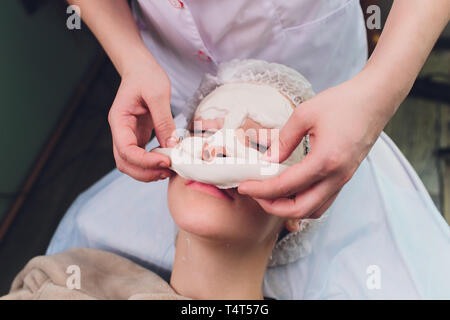 Facial procedures. Nice skilled cosmetician taking off a mask while doing a beauty procedure Stock Photo
