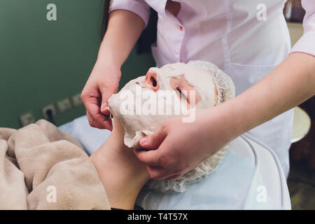 Facial procedures. Nice skilled cosmetician taking off a mask while doing a beauty procedure Stock Photo