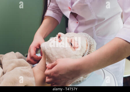 Facial procedures. Nice skilled cosmetician taking off a mask while doing a beauty procedure Stock Photo