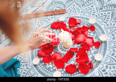 Dance of female hands with mehendi over the altar of candles and rose petals, women practices Stock Photo