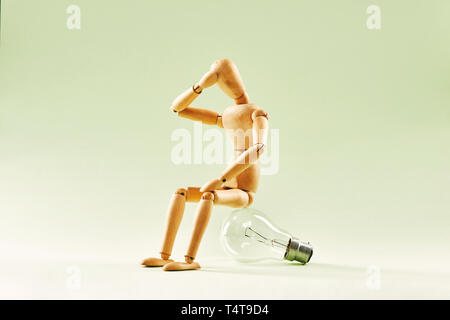 Having no idea. Wood figure mannequin sitting on an incandescent light bulb Stock Photo