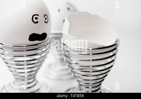 Three anthropomorph chicken eggs in silver egg cups, one broken egg. Stock Photo