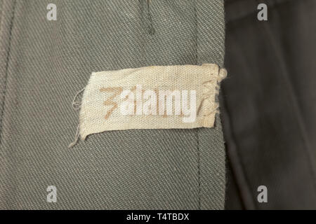 A summer field tunic of an SS-Hauptsturmführer of the infantry found in Normandy Light field-grey cotton cloth with dark-green collar and metal buttons, unlined version with integrated hanger (shortened) and opening for the sidearm, Iron Cross ribbon, orders loops. The side darts have been let out. The collar and collar patches with moth holes. Black collar patches with runes embroidered in silver and silver cord trim. Sewn-on shoulder boards with black lining and white branch colour. The silhouette of the sleeve eagle still visible. Worn tunic bleached by the sun, with tra, Editorial-Use-Only Stock Photo