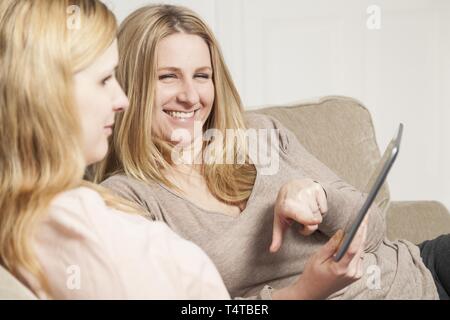 Two women sitting on a sofa and looking into a Tablet PC Stock Photo
