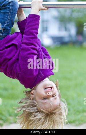 Girl, five years, hanging upside down on a horizontal bar, Kiel, Germany, Europe Stock Photo