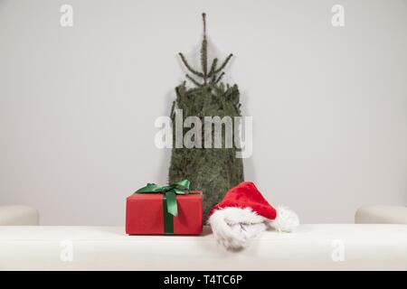 Christmas gift and Christmas hat lying on a sofa, behind a packaged Christmas tree Stock Photo